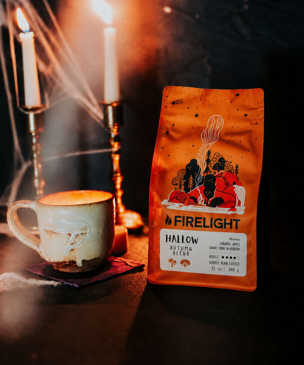 Hallow Autumn Blend bag next to a mug of coffee and candlelight